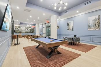 A pool table is in the middle of a room with a blue wall and a painting of a cityscape. at LiveWell Apartments, Pennsylvania